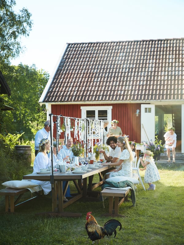 Familie og venner samles rundt et NORRMANSÖ-bord i hagen, deler mat og nyter sankthansaften.