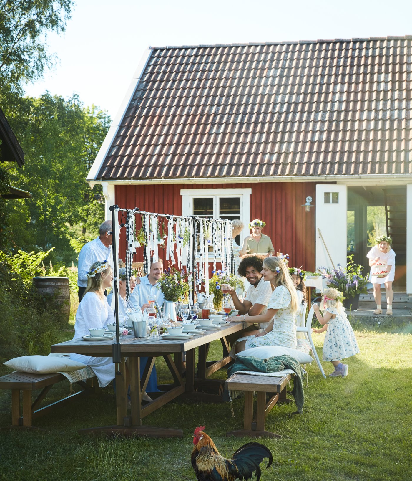 Family and friends gather around a NORRMANSÖ table in the garden, sharing food and enjoying midsummer eve.