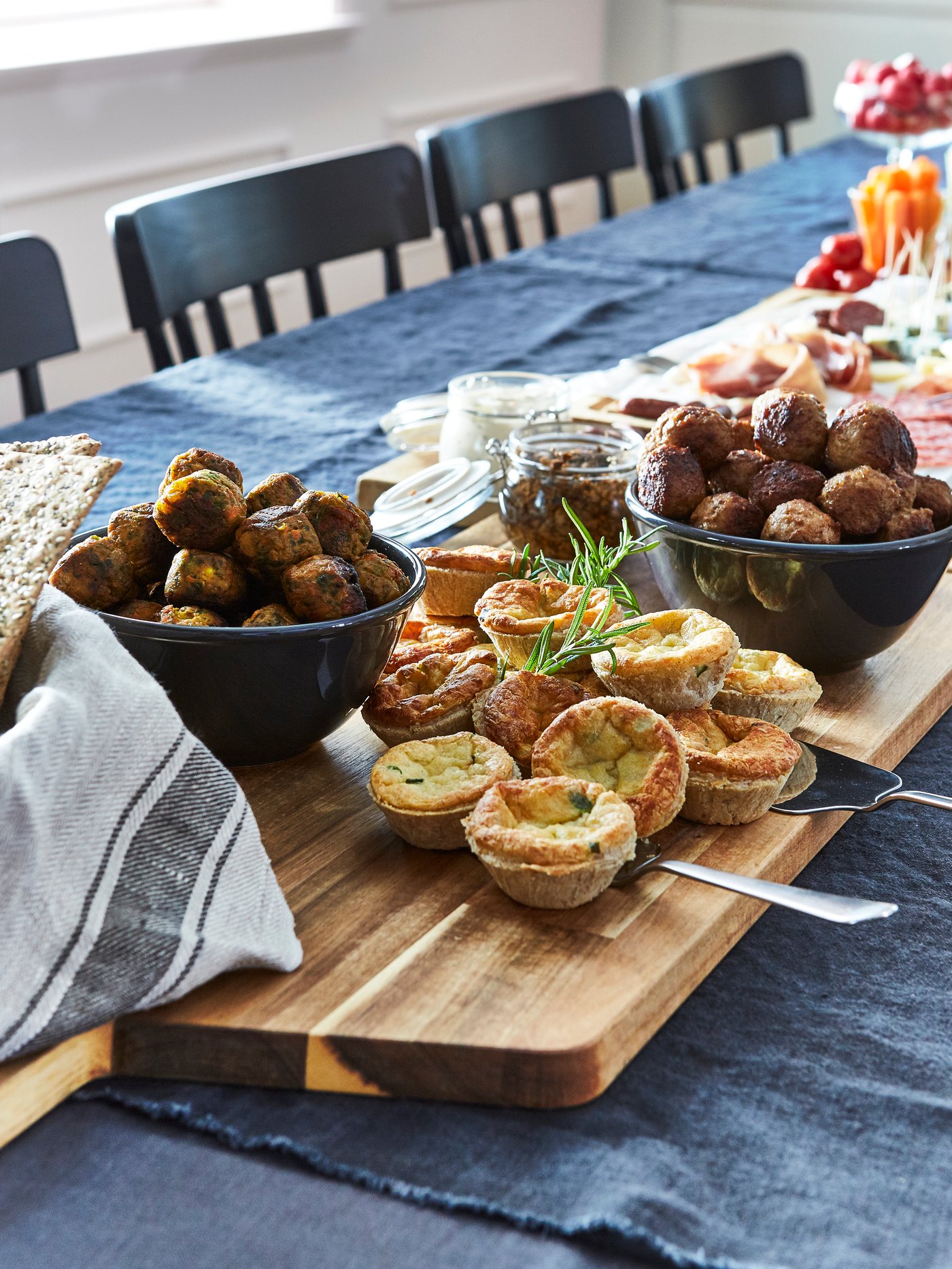Una tabla para picoteo SMÅÄTA con mini quiche y pocillos con falafell sobre una mesa de comedor con mantel negro.