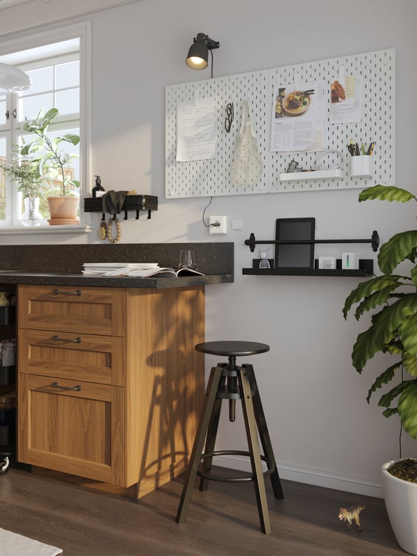 Un tabouret de bar DALFRED noir au bout d’un comptoir de cuisine avec une étagère noire et un tableau-mémo blanc sur le mur derrière.