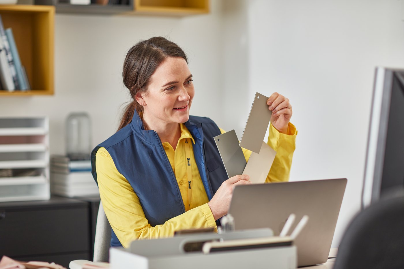 IKEA coworker on front of a laptop holding up paint swatches to the screen