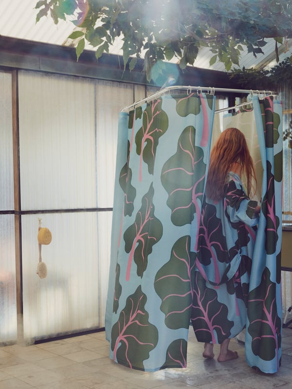Una donna che indossa un kimono BASTUA con motivo a foglia entra in una sauna con tende doccia BASTUA.