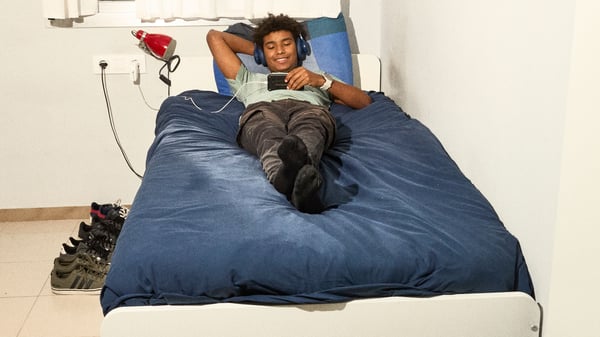 Man smiling in bed while laying down watching his phone.