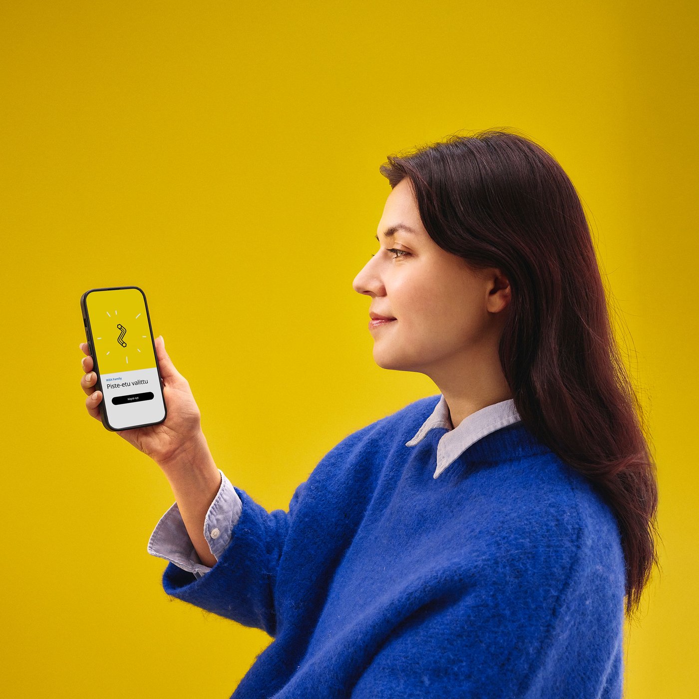 En kvinna med en blå skjorta håller i en mobiltelefon i handen mot en gul bakgrund.