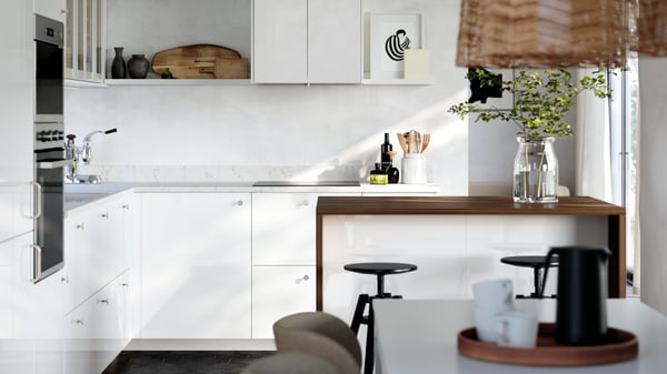 A kitchen with white high-gloss RINGHULT fronts and HEJSTA glass doors has a picture ledge on the wall and a kitchen island.