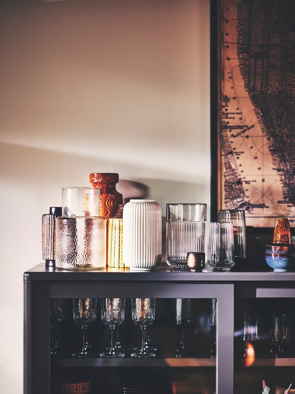 A KONSTFULL vase, a white STILREN vase, and a GRADVIS vase with metal insert, on an IDÅSEN cabinet with sliding glass doors.