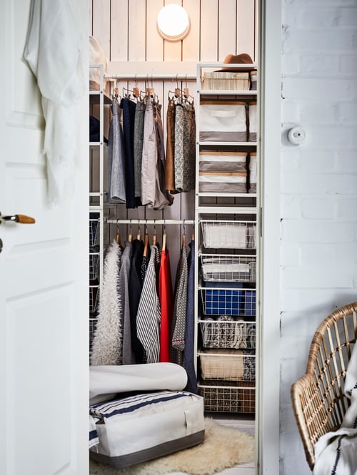 A JONAXEL storage system seen through an open door, with clothes on hangers and other items of clothing in metal baskets.