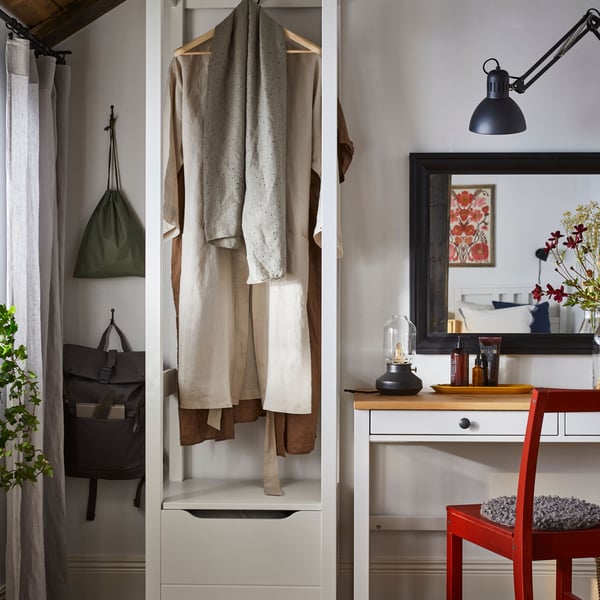 A white stain/light brown HEMNES desk with two drawers and a desk lamp on top is placed against a wall with a mirror.