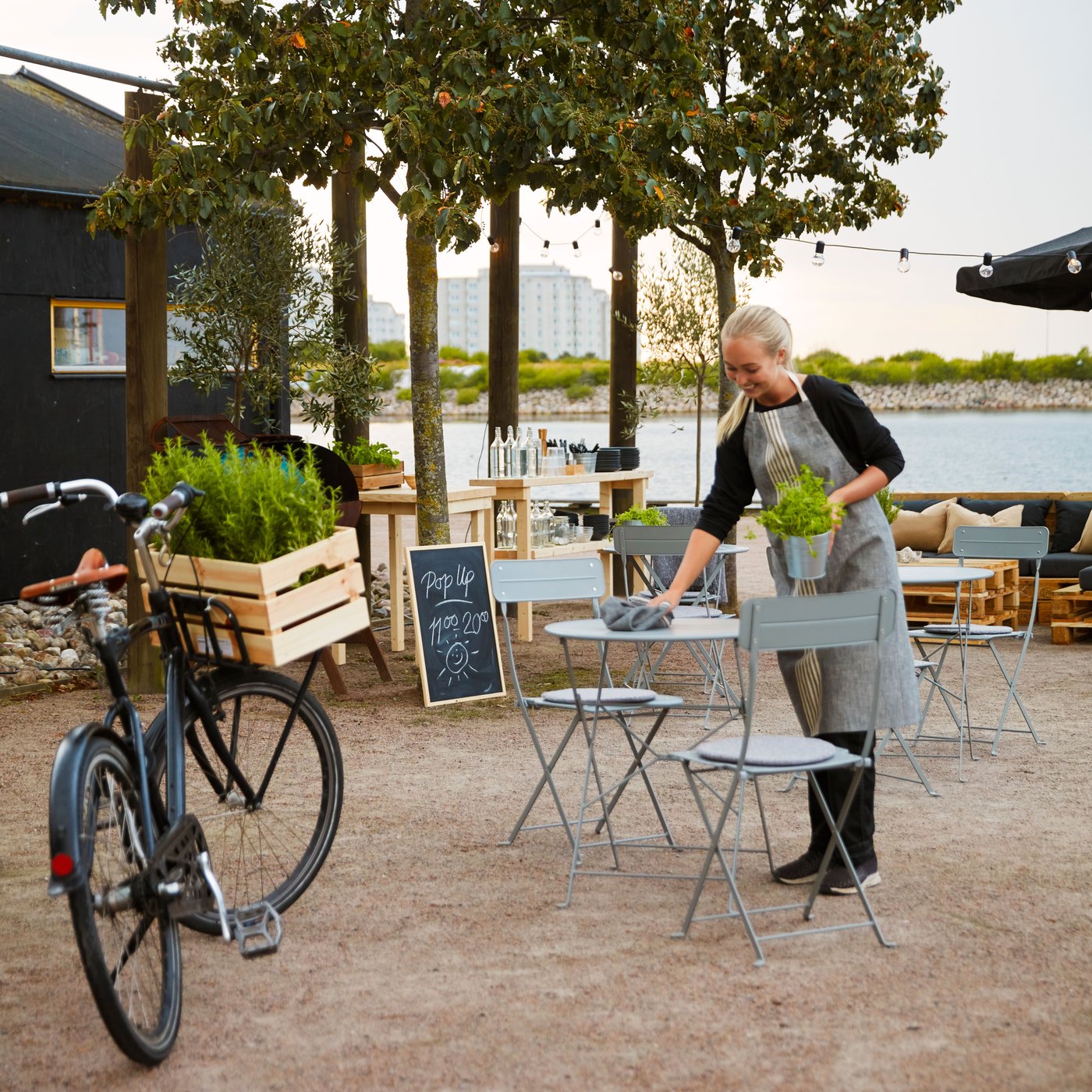 A waitress at an outdoor seating is cleaning a grey SUNDSÖ table.