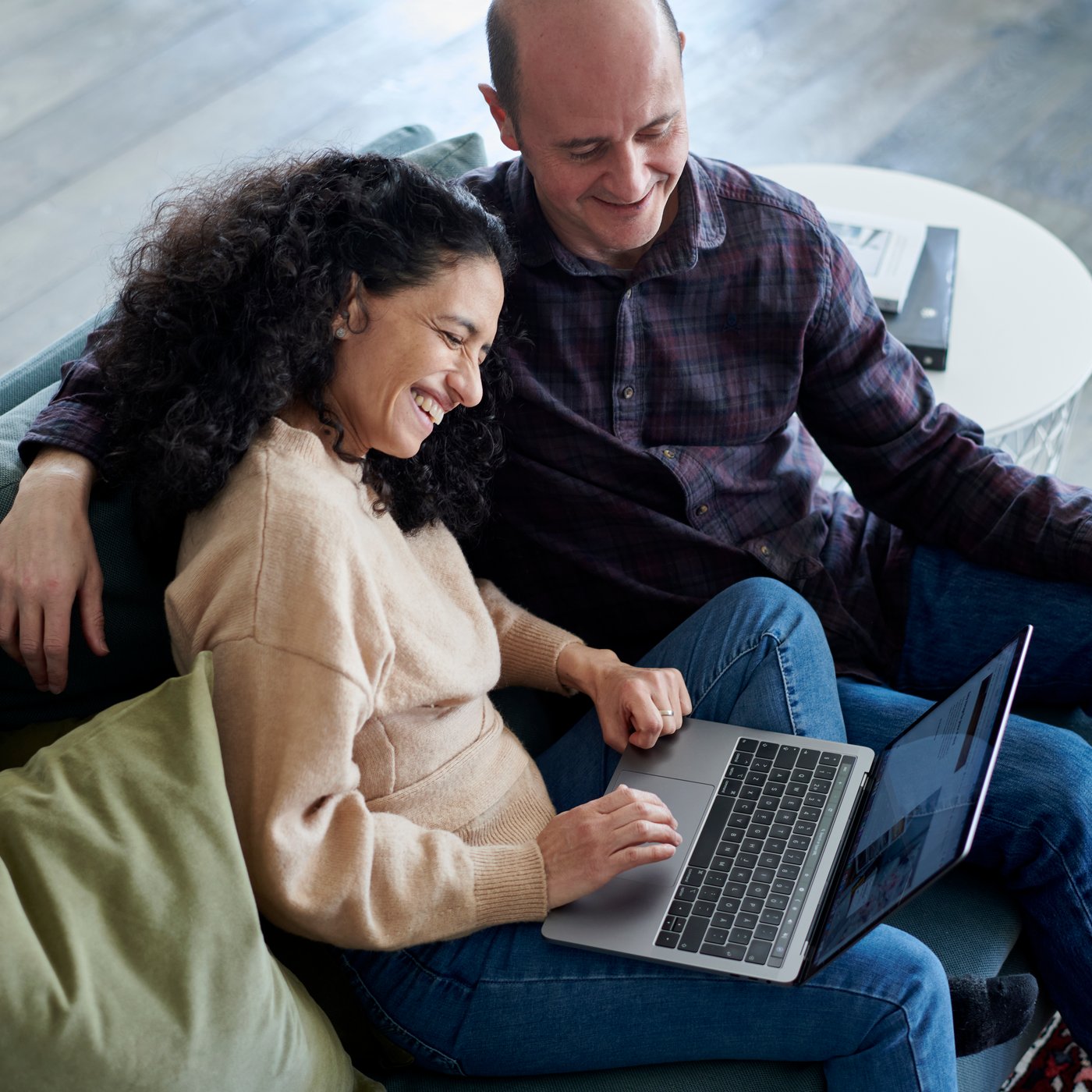 Zwei Personen sitzen auf einem Sofa und schauen lächelnd in einen Laptop.