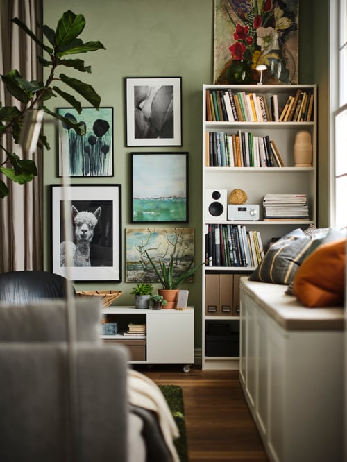 A living area with a white PLATSA storage bench, white BILLY bookcase and a gallery wall.