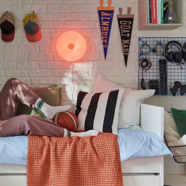 A bedroom featuring a VARMBLIXT lamp mounted on a white brick wall, a bed frame, with patterned cushions and a basketball.