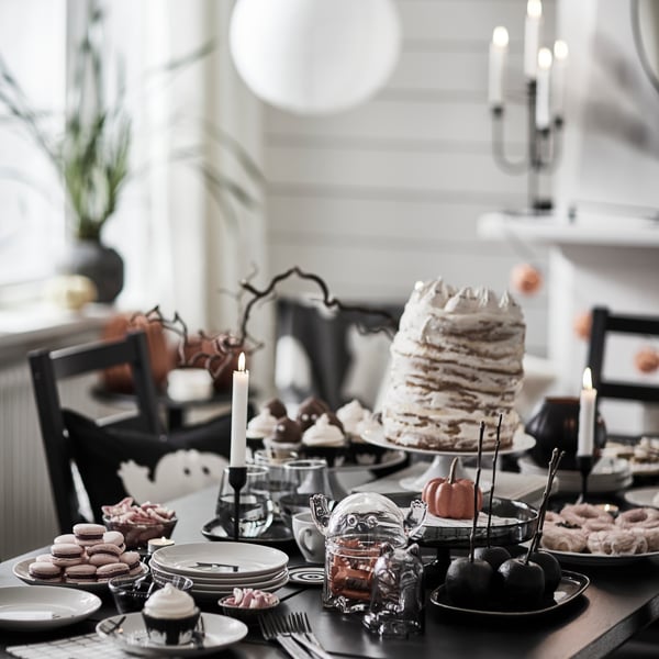 A dark table with KUSTFYR side tables, several treats, a KUSTFYR bowl with lid shaped like a ghost and some lit candles.