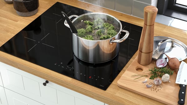 Das Bild zeigt eine moderne Küchenszene aus der Vogelperspektive. Im Mittelpunkt befindet sich ein MATMÄSSIG Induktionskochfeld der Serie IKEA 300. Das Kochfeld ist in eine helle Holzarbeitsplatte eingelassen, die warm wirkt und einen natürlichen Kontrast zur dunklen Kochfläche bildet.