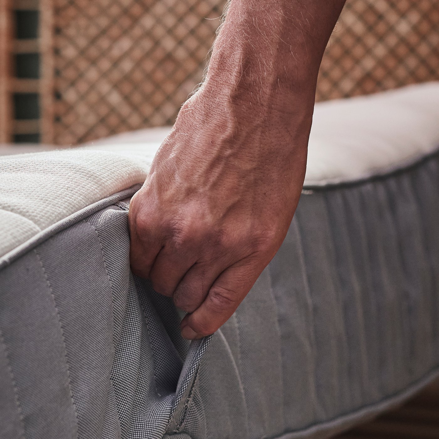 Eine Person greift eine hellblaue feste VALEVÅG Taschenfederkernmatratze an einer seitlich befestigten Schlaufe.