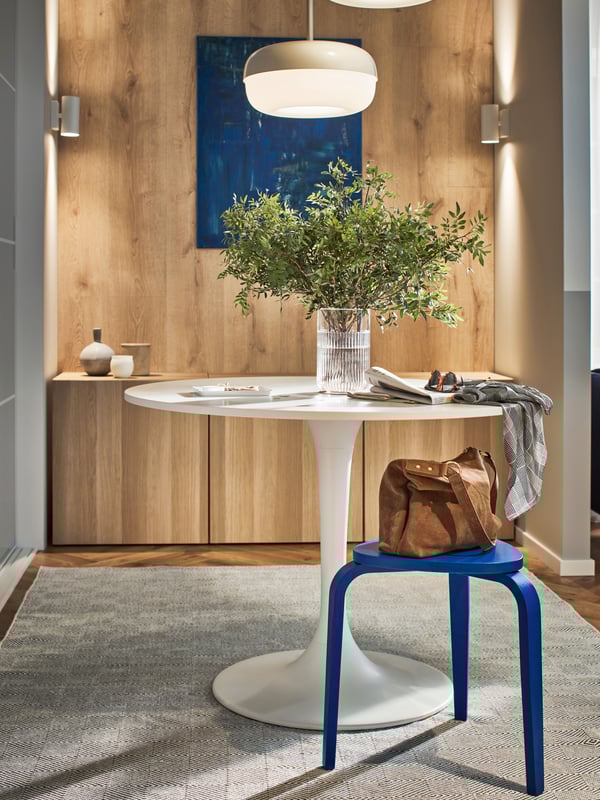 A round white DOCKSTA table in front of a white stained oak effect BESTÅ cabinet combination and on top of a GÅNGVÄG rug.