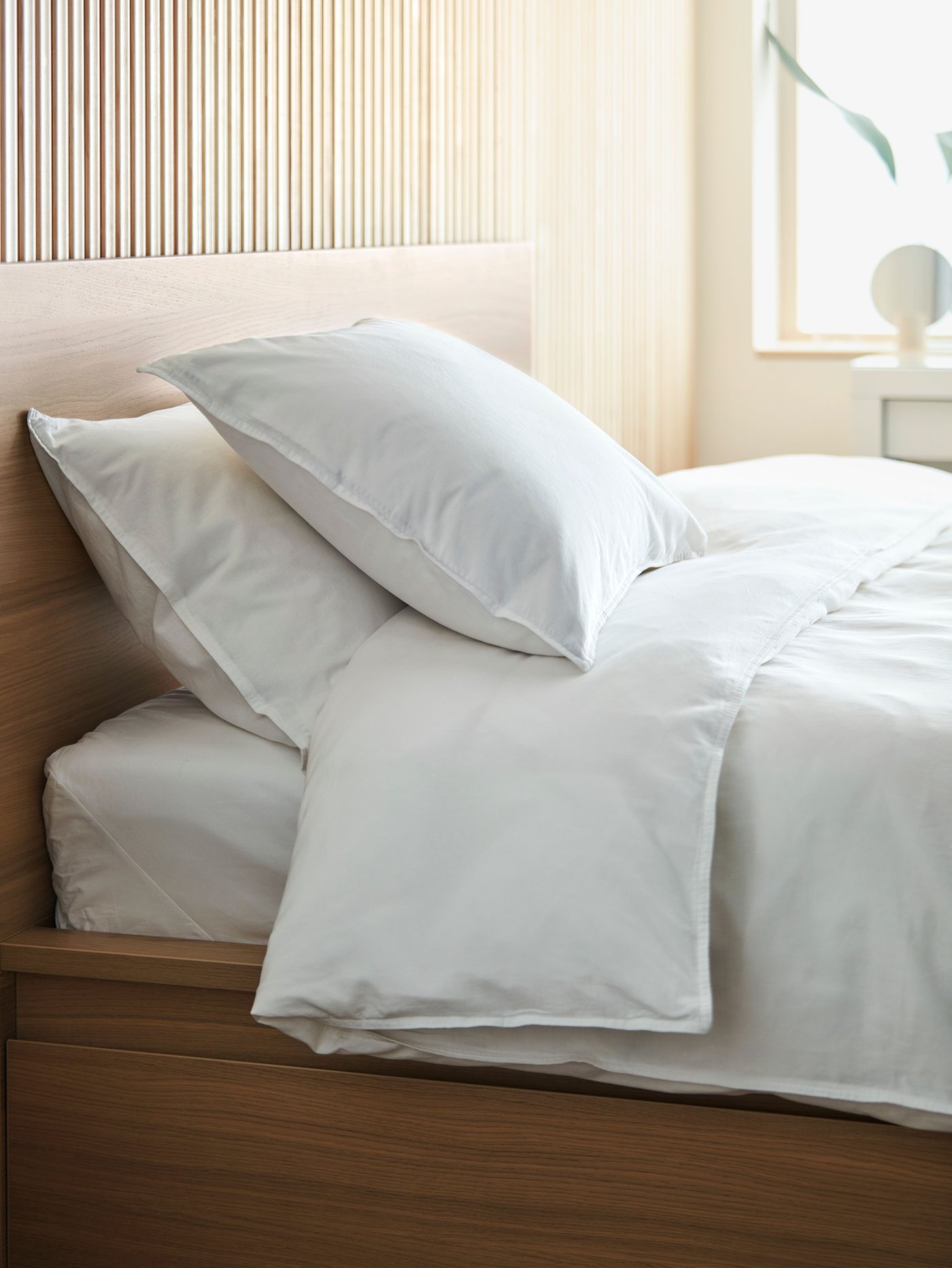 صورة مقربة لسرير عليه شراشف ووسادات ناعمتان باللون الأبيض الناصع وضوء النهار يسطع من خلال النافذة في الخلف.