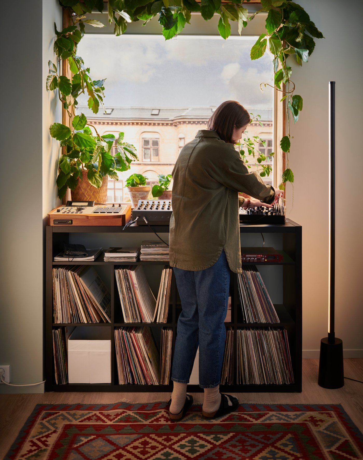 A black OBEGRÄNSAD record bag with vinyls inside sitting on a wooden floor next to shelves of records and a white curtain.