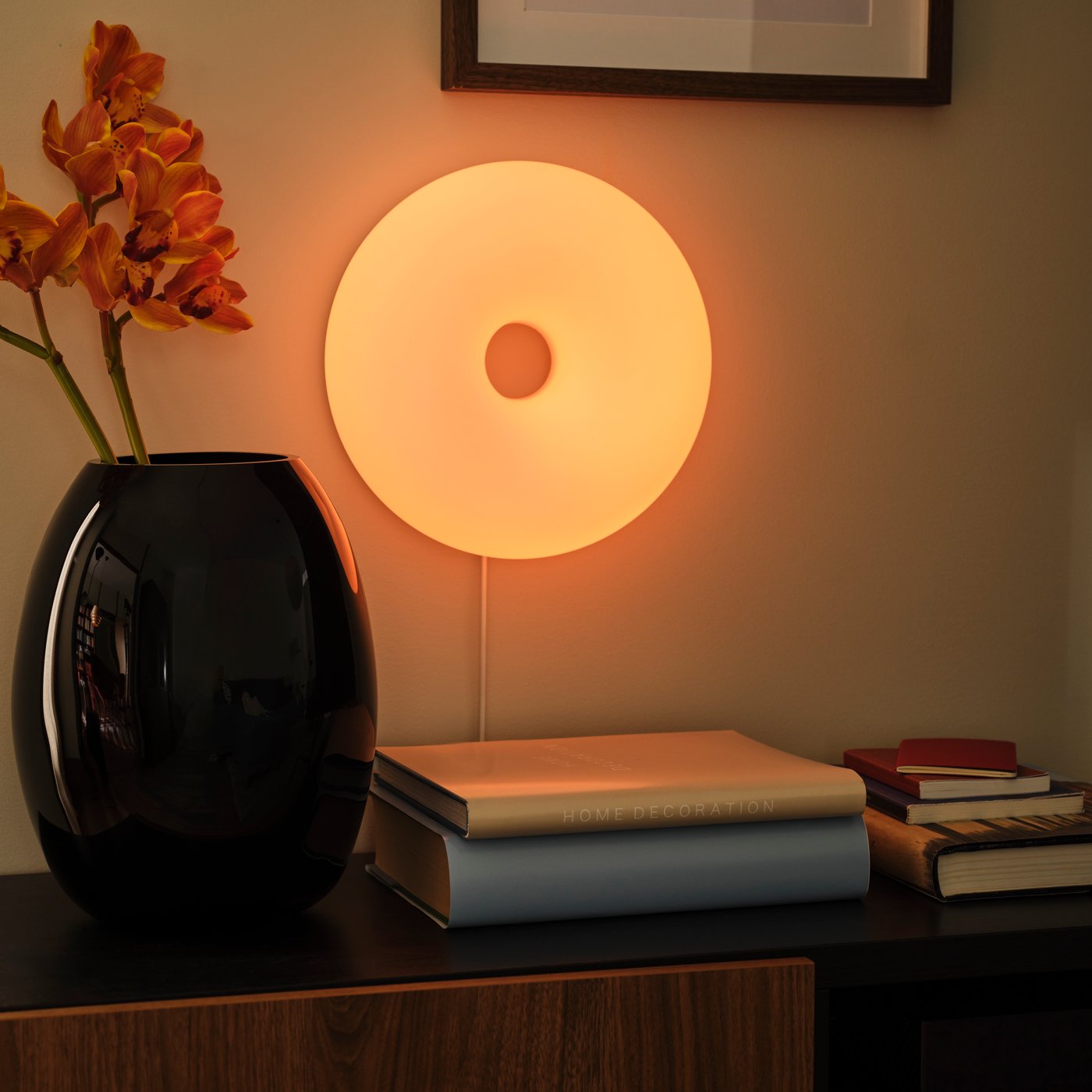 A VARMBLIXT LED table/wall lamp is mounted on the wall above a BESTÅ TV bench. A black vase stands on the TV bench.