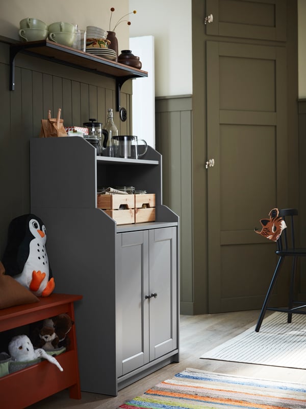 A grey HAUGA cabinet with 2 doors stands against a wall next to a red-painted PERJOHAN bench with storage.