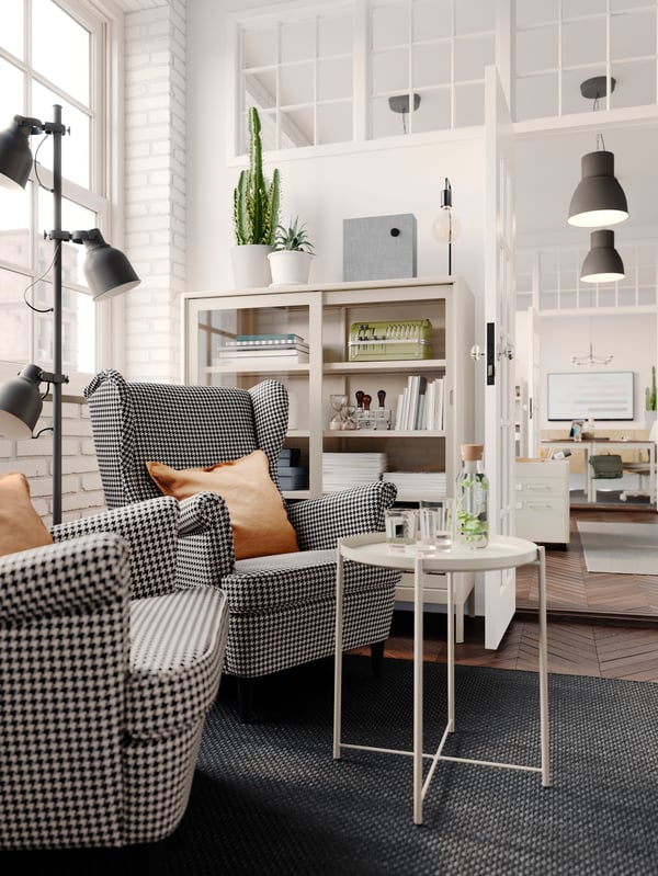A light office interior with two black-and-beige-chequer STRANDMON armchairs next to refreshments on a GLADOM tray table.