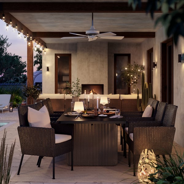 An outdoor dining setup in evening light, featuring six dark grey VITTSKÄR dining chairs with pillows and a matching table.
