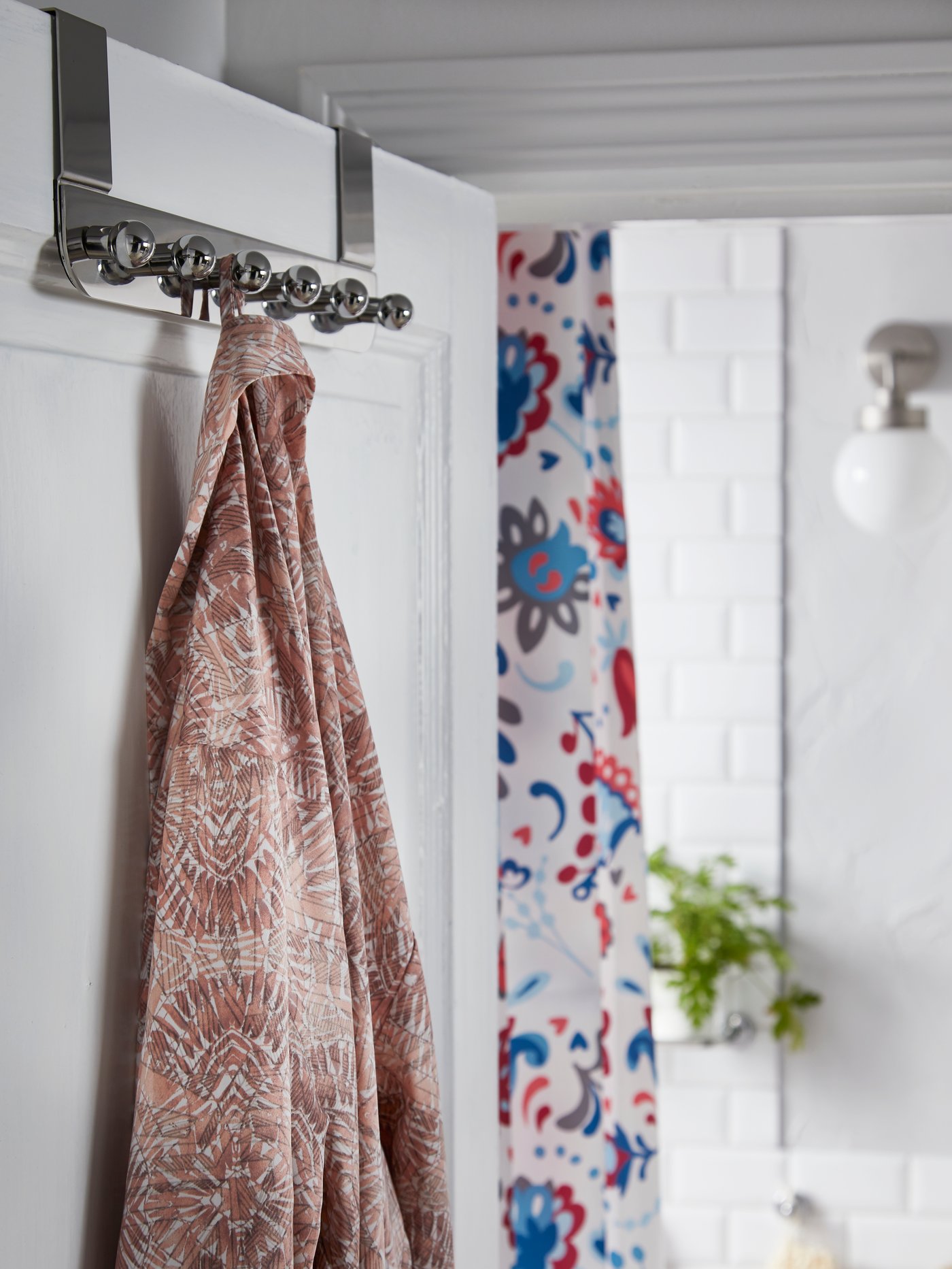 Penyangkut VOXNAN untuk pintu dalam kesan krom digantung pada pintu bilik mandi dan jubah mandi bercorak digantung padanya.