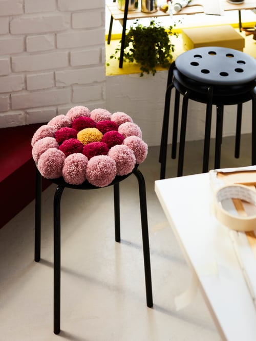 Dining room area featuring a stack of two MARIUS stools, a stool with a flower-shaped cushion, and the corner of a table.