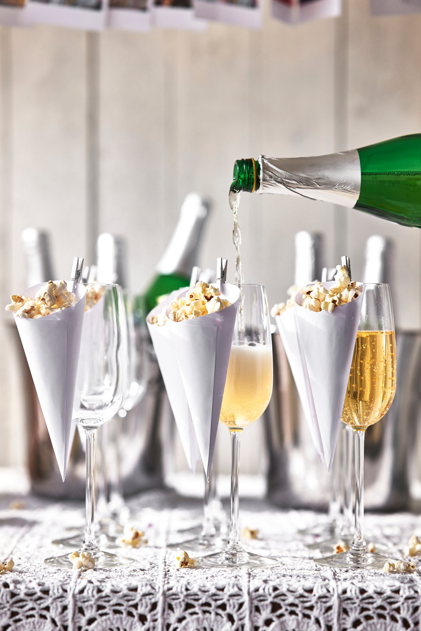 Champagne hälls upp i ett glas bredvid andra glas fyllda med popcorn i vita strutar, förberett för ett festligt firande.