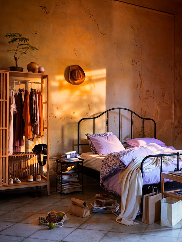 A black bed with a steel frame and brass-coloured details. The bed is placed against an orange wall on a tiled floor.