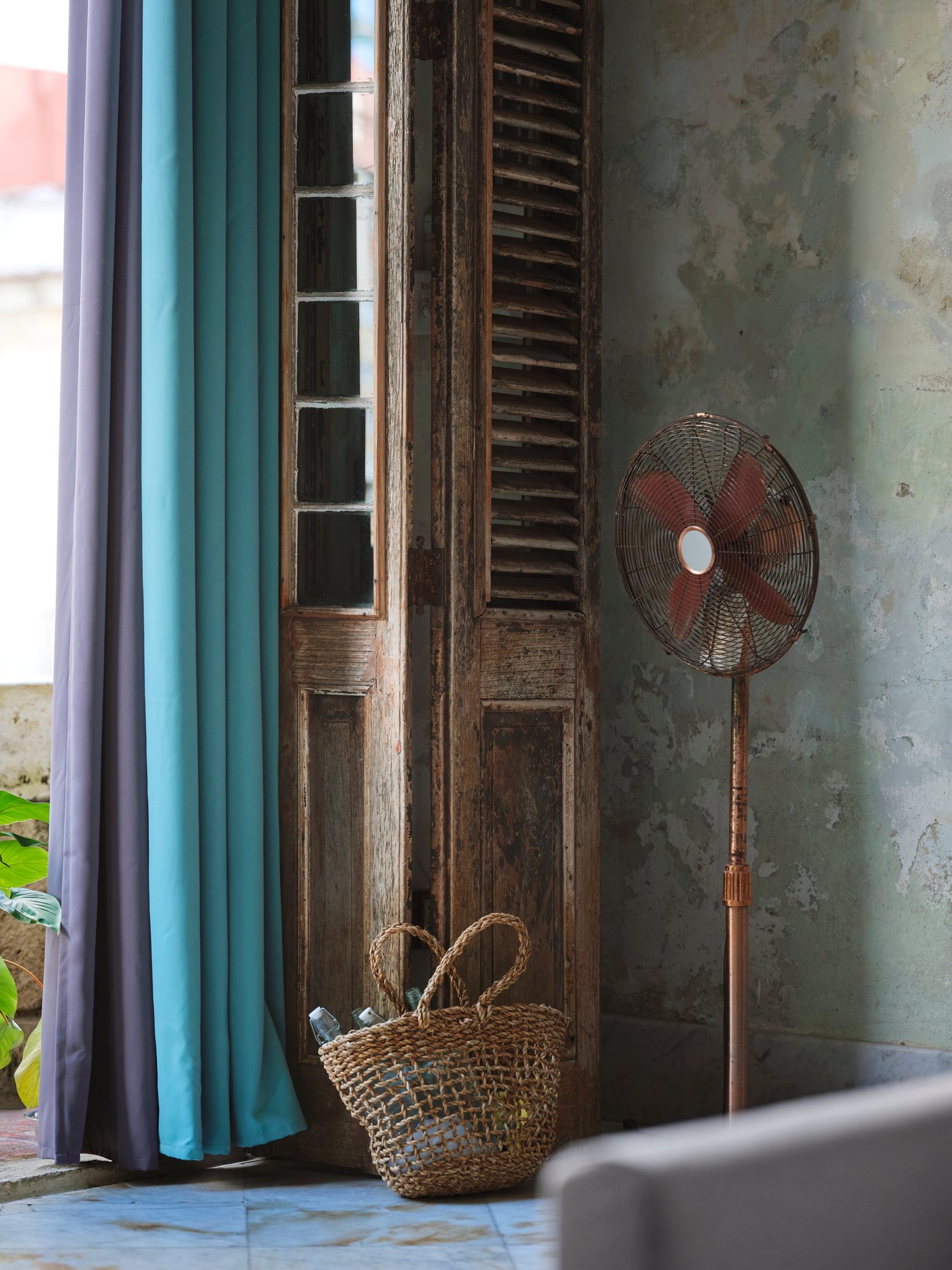 Purple and turquoise block out curtains hanging against an open, wooden door with a woven basket placed next to it.