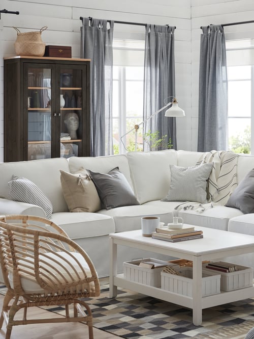 Living room with sofa, armchair, coffee table, floor lamp, throw, cushion covers, basket, storage unit, mug, books, curtains.