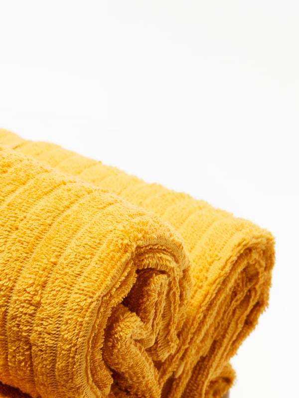 A closeup of two tightly rolled-up yellow VÅGSJÖN towels against a white background.