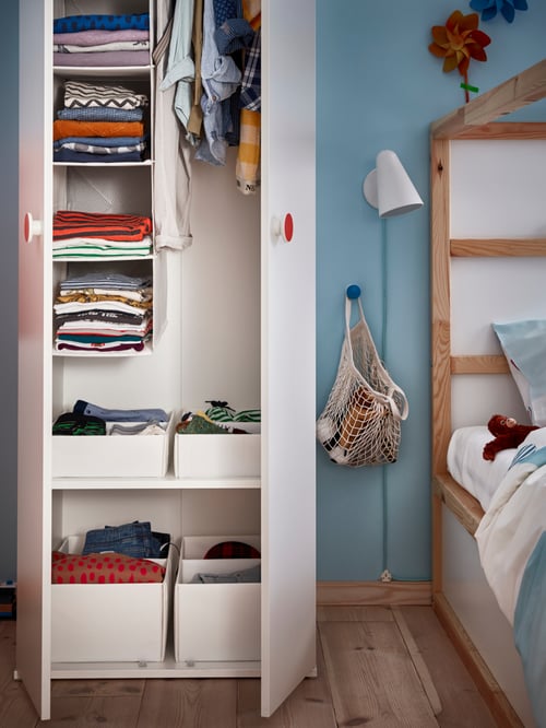 GODISHUS wardrobe in a blue bedroom next to a bed. The wardrobe is open and filled with folded and hanging clothes.