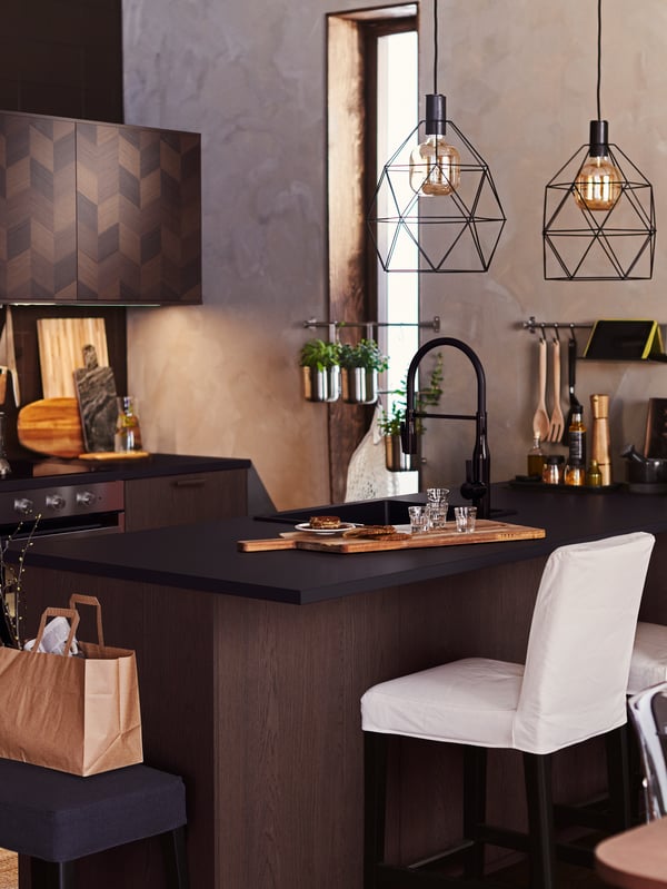 A kitchen with a BERGMUND bar stool, a kitchen island with various items and black BRUNSTA pendant lamps and bulbs.