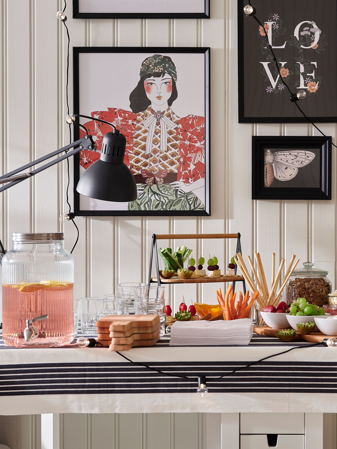 Dukat bord med dryck, kakor, frukt och grönsaker. I bakgrunden syns tavlor och ljusslingor på väggen.