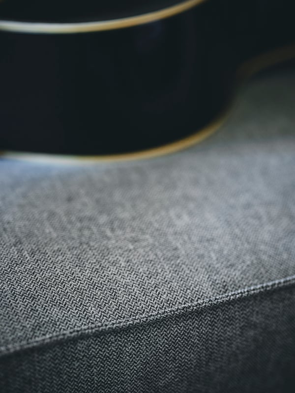 Un primo piano di una fodera per divano KIVIK beige-grigio mostra i bordi in rilievo e la trama con forma a V che crea un effetto bicolore.