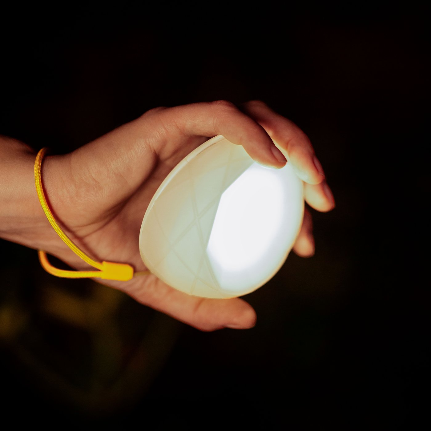 Gambar dari dekat tangan seseorang memegang pencahayaan berkuasa solar LED SAMMANLÄNKAD dengan tali berwarna kuning di sekeliling pergelangan tangan.