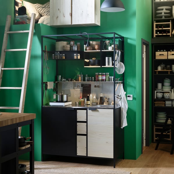An ÄSPINGE kitchenette with utensils, spices, and more sits against a green wall next to a ladder leading to a sleeping loft.