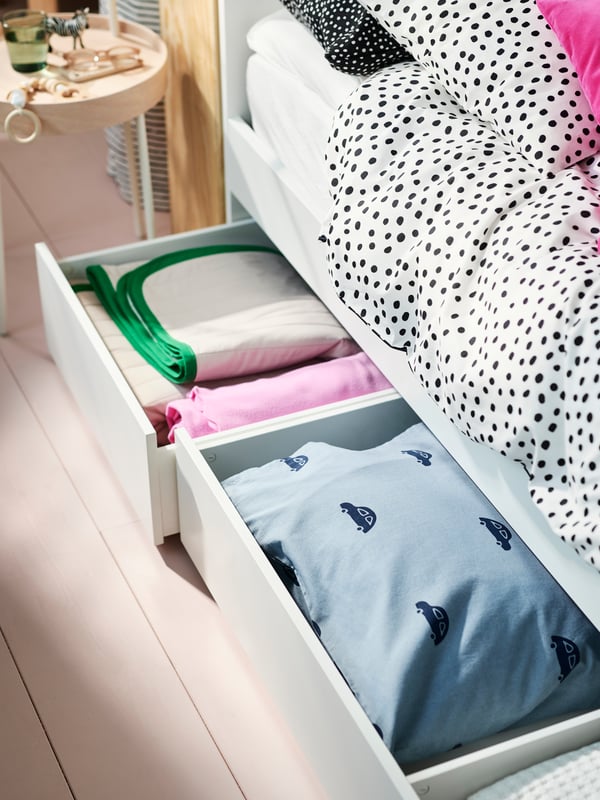 A white VIHALs double bed covered in BJÖRKGRÅMAL bed linen with two storage drawers open holding folded bed linen.