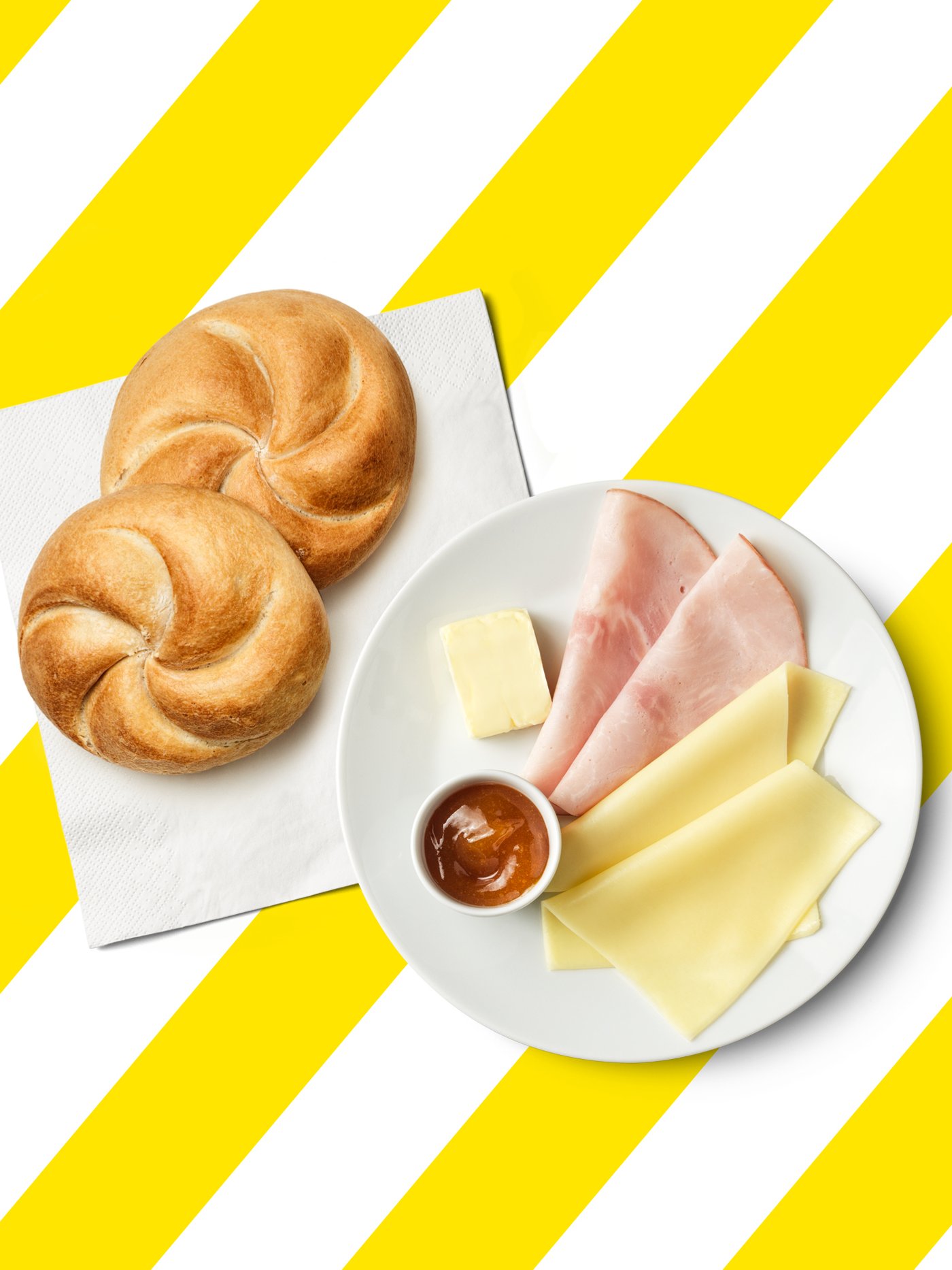 Ein Frühstücksteller mit einer Semmel, Käse, Schinken, Butter und Marmelade.