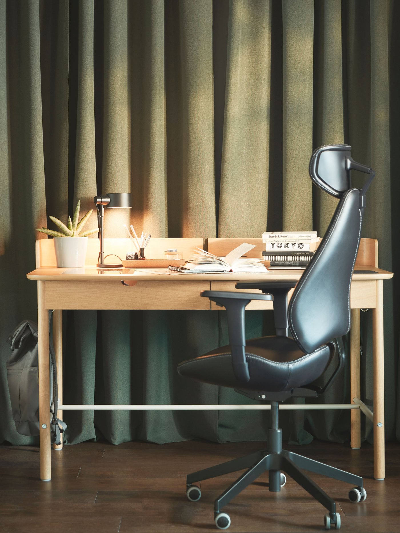 Es ist ein Arbeitsplatz mit einem GRUPPSPEL Gamingstuhl und einem RIDSPÖ Schreibtisch aus Eichenfurnier vor bodenlagen ROSENMANDEL Gardinen in Dunkelgrün zu sehen.