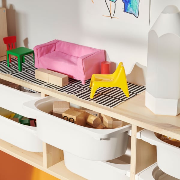 Various colourful toys on top a light white stained pine TROFAST wall storage filled with white storage boxes.