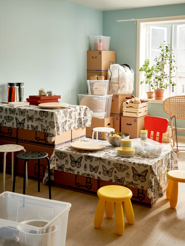 Mehrere Umzugskartons werden als Tisch benutzt und sind mit einer Tischdecke dekoriert.