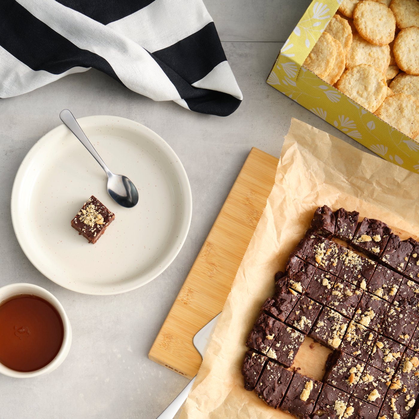 Des biscuits à l’avoine BJÄLLRA bruns soigneusement disposés près d’un fudge au chocolat et d’une tasse de thé, sur un comptoir de cuisine.