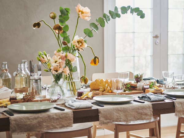 Långt MÖRBYLÅNGA bord med bitar av AINA metervara, FÄRGKLAR tallrikar, blommor i vaser samt olika dekorationer.