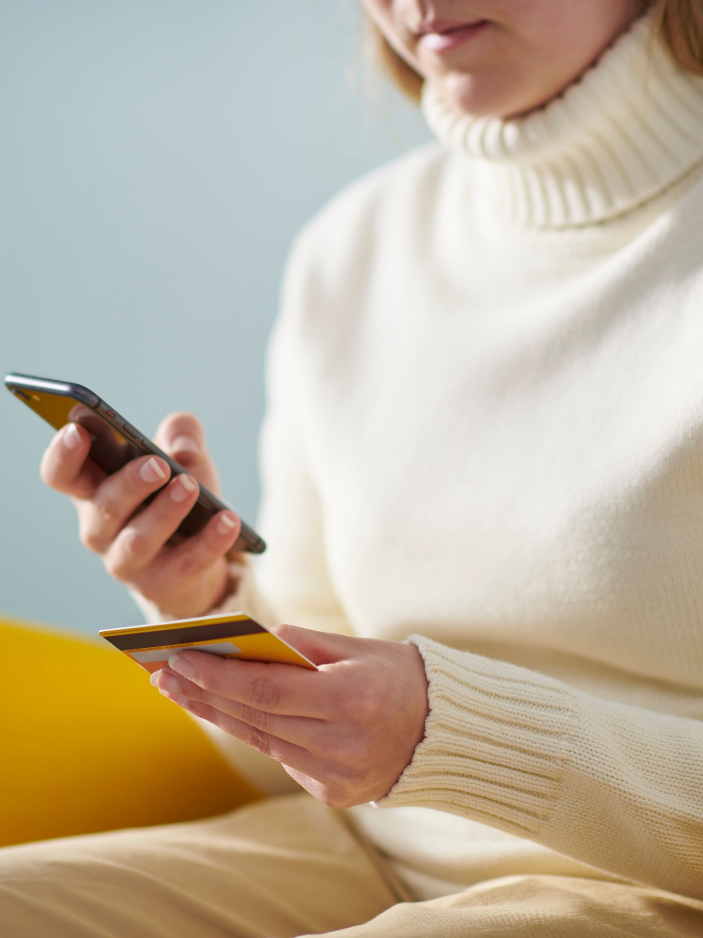 Woman on mobile phone and credit card in hand. Sat in a yellow poang. 