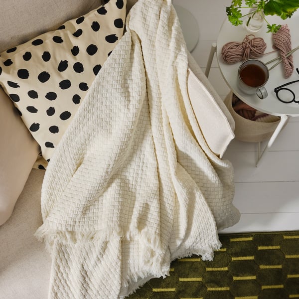 Manta HORNMAL blanca color hueso junto a cojín blanco con puntos negros.