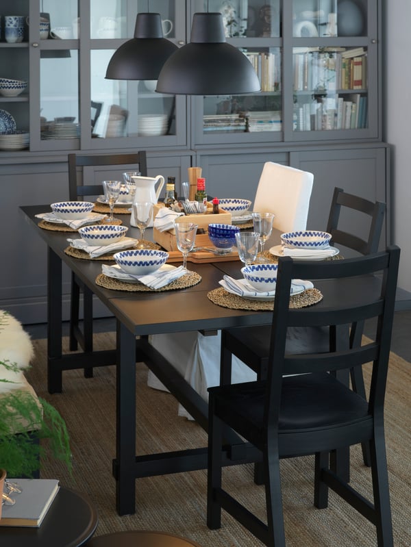 Comedor con una mesa extendida y sillas en negro. La mesa está puesta para la cena con dos lámparas de techo negras en la parte superior.