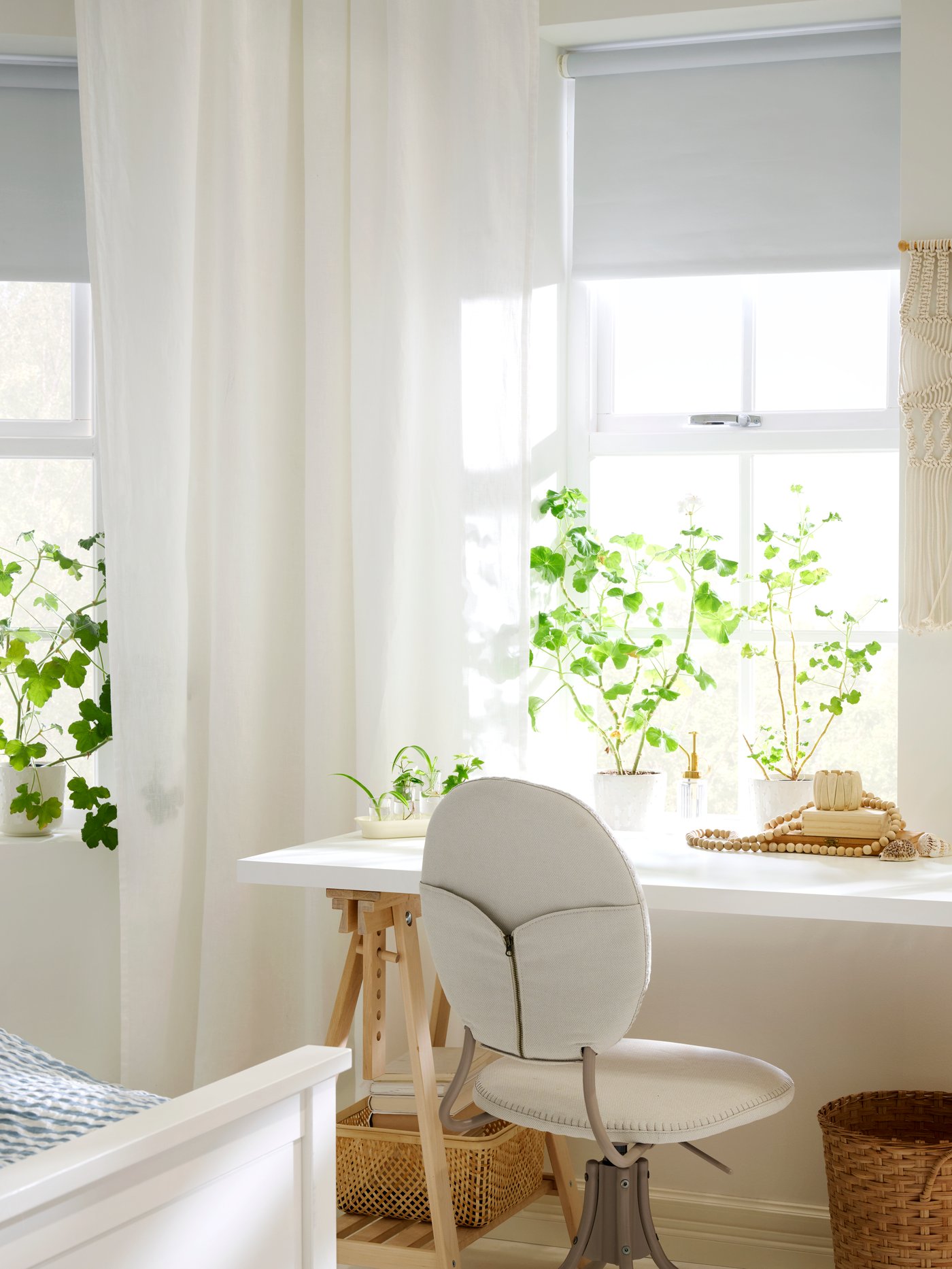 A light bedroom with windows in the back, a desk and office chair, sheer white curtains and FRIDANS block-out roller blind.